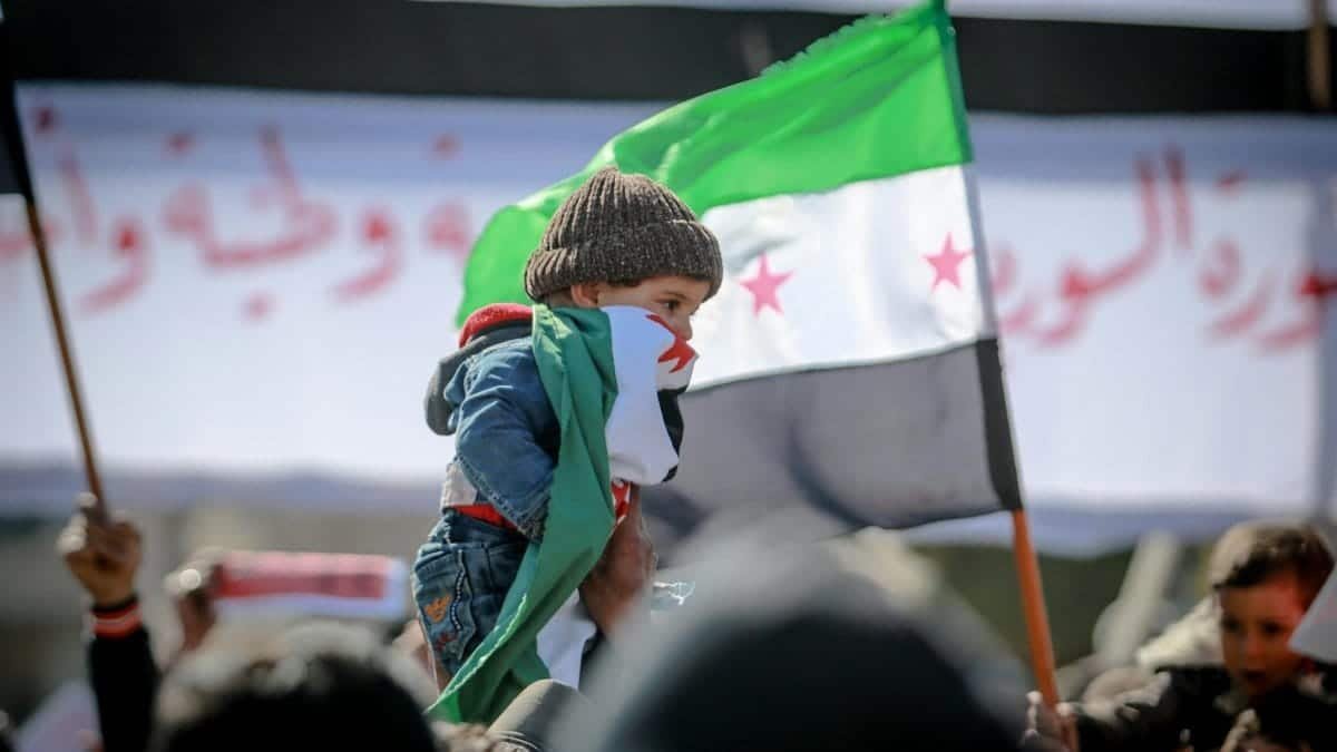 Child with Syrian flag at protest, symbolizing hope and innocence amidst adversity.