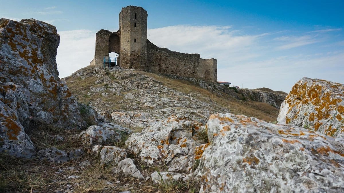 Explore the historic castle ruins perched on a rocky hill, surrounded by a vivid blue sky.
