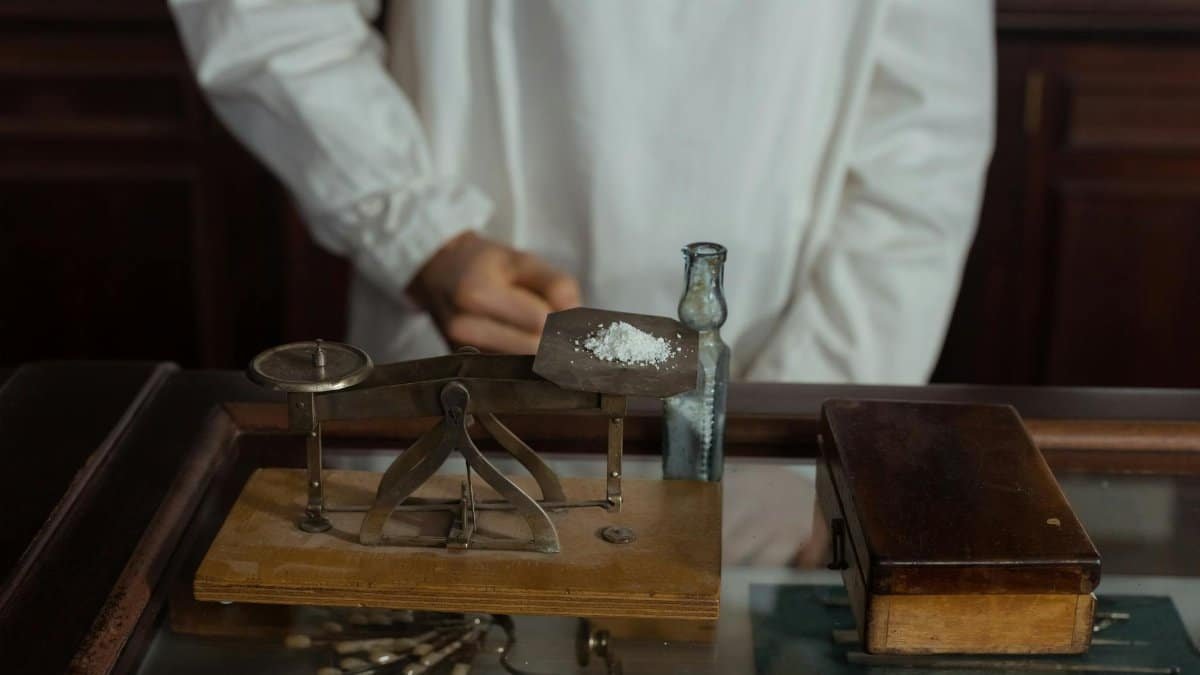 A pharmacist in a white gown working with a vintage scale and medicine bottle, showcasing retro pharmacology tools.