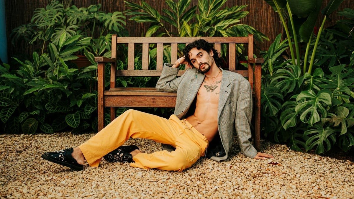 Stylish model relaxing on bench, showcasing contemporary fashion amidst lush greenery.