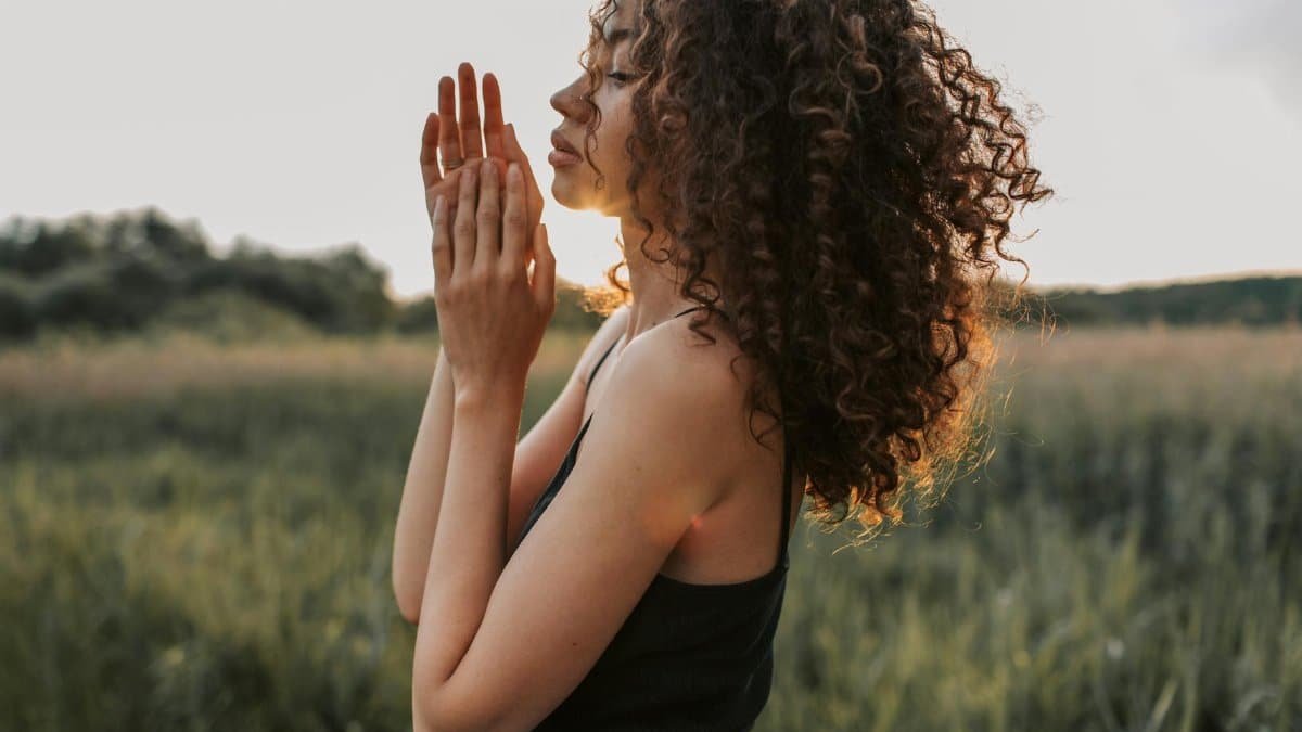 A woman with curly hair enjoys a peaceful moment in a sunlit field, embracing nature.