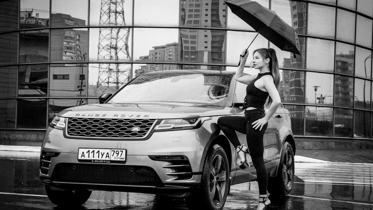 Stylish model poses with a luxury car during a rainy urban shoot.