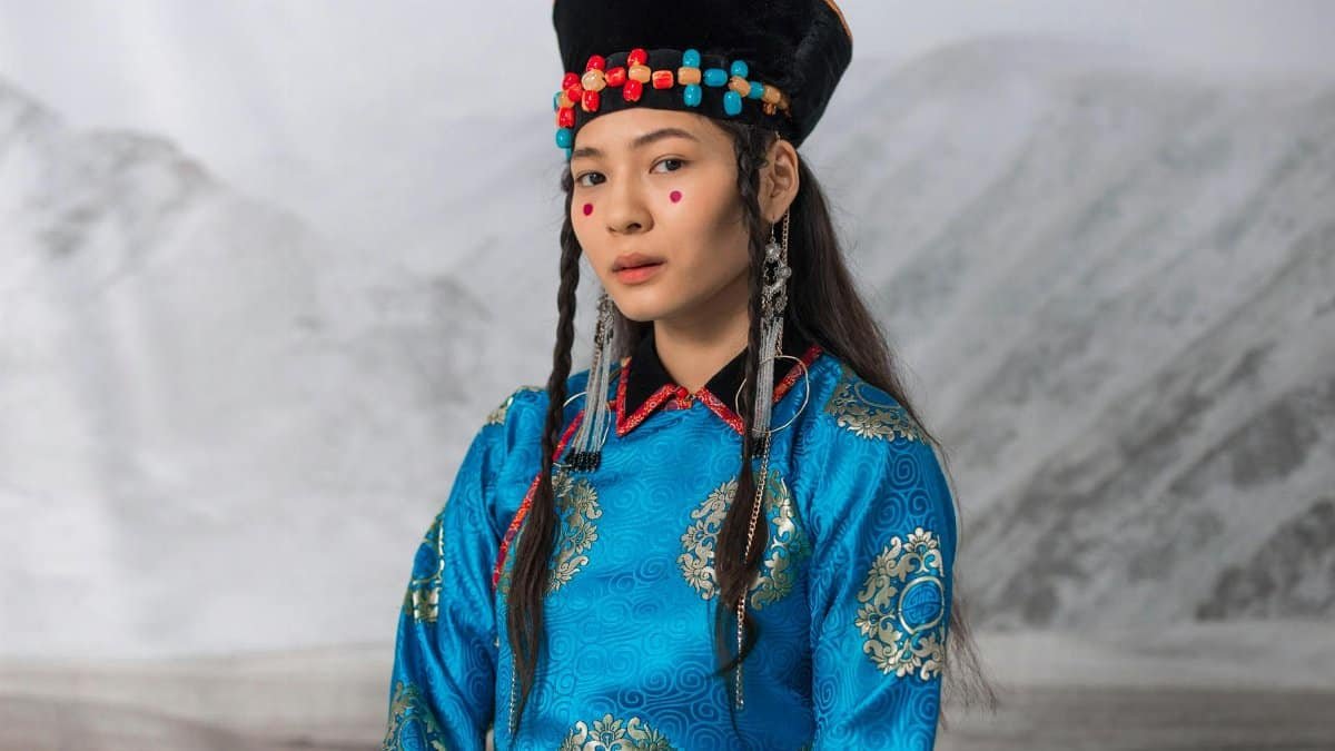 Portrait of a woman in traditional Mongolian dress and colorful headwear in a serene setting.