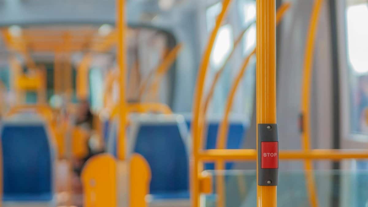 Red stop button on yellow handrail in modern empty public bus during daytime