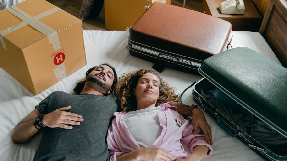 A young couple relaxes on a bed surrounded by packed boxes and suitcases, symbolizing a new beginning.