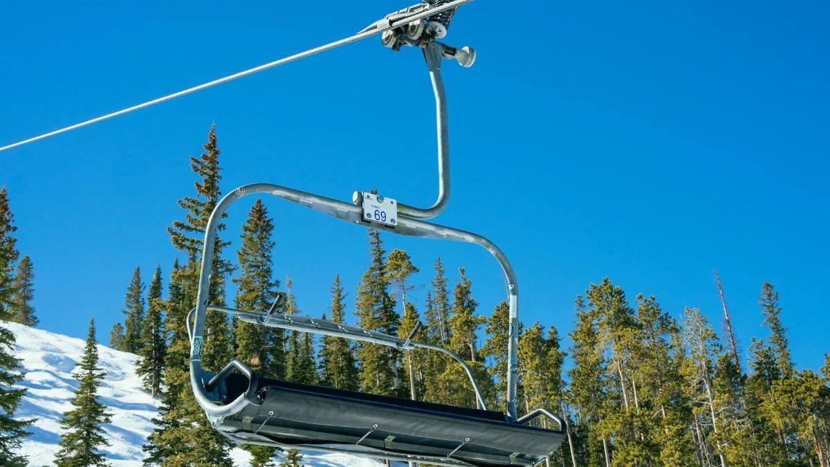 An empty ski chairlift against a clear blue sky with snow-covered pines below, capturing the serene winter scene.
