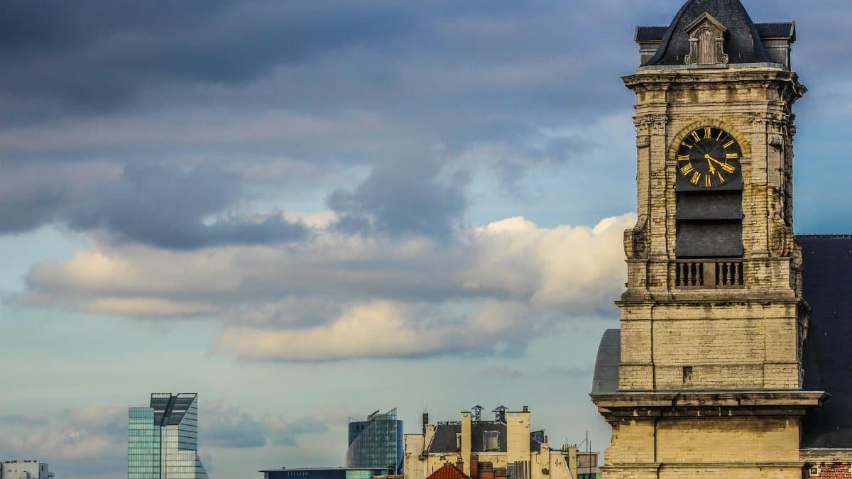 Historic clock tower against urban skyline under cloudy sky. Captivating blend of old and new architecture.
