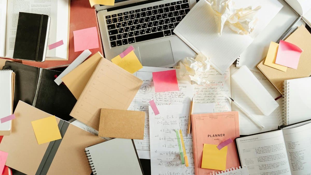 Flatlay of a messy study desk with laptop, notebooks, and sticky notes, showcasing the creative process.