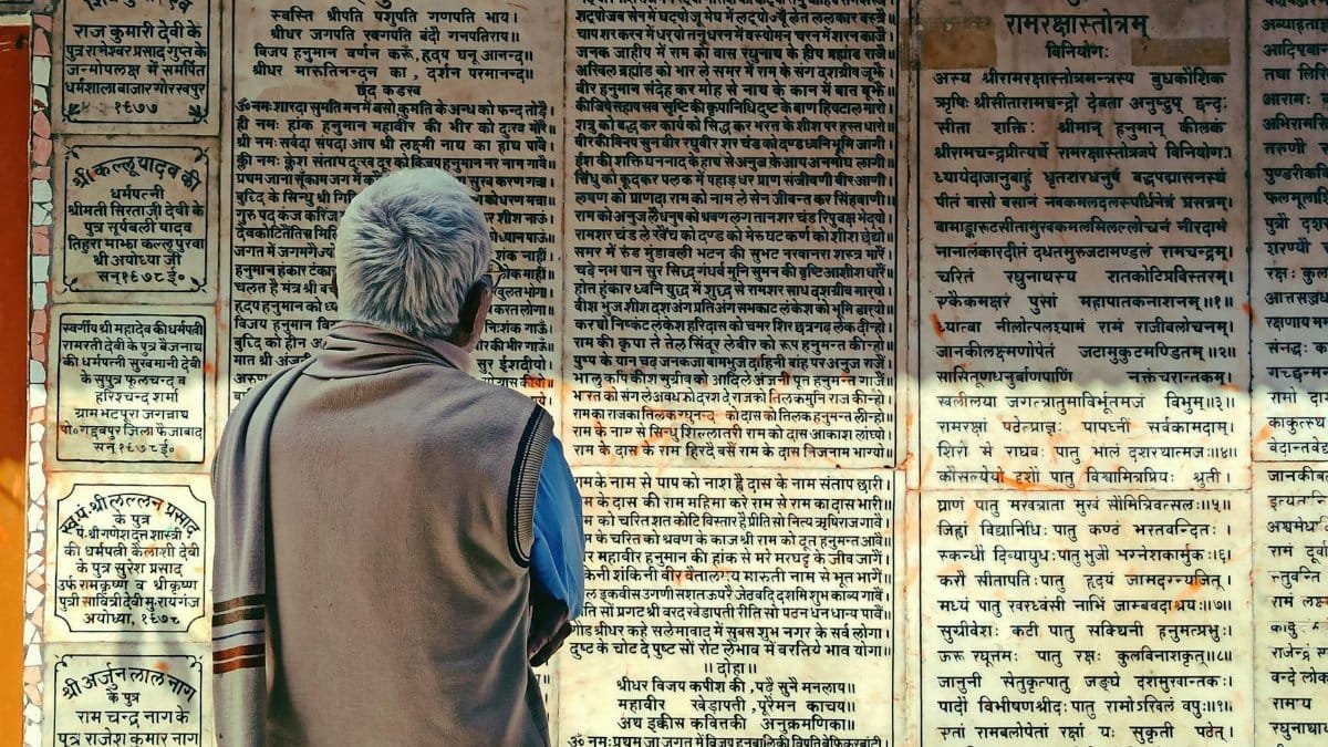 Elderly man reads ancient scriptures on temple wall in Bodh Gaya, India, rich in cultural heritage.