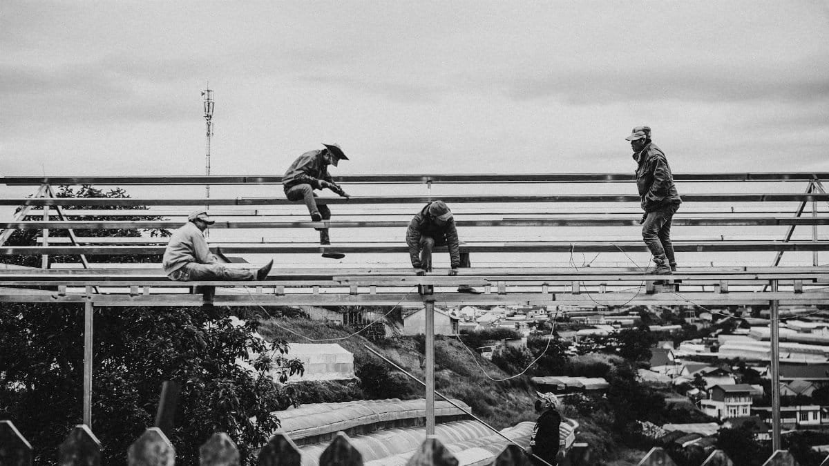 Black and white image of workers on a metal framework with a city backdrop.