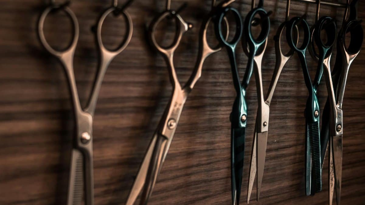 A collection of vintage barber scissors hanging on a wooden wall, showcasing sharp tools for hair cutting.