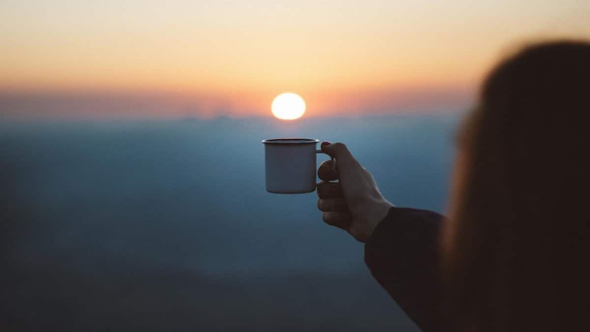 A person holds a coffee cup against a beautiful sunrise, capturing a serene outdoor moment.