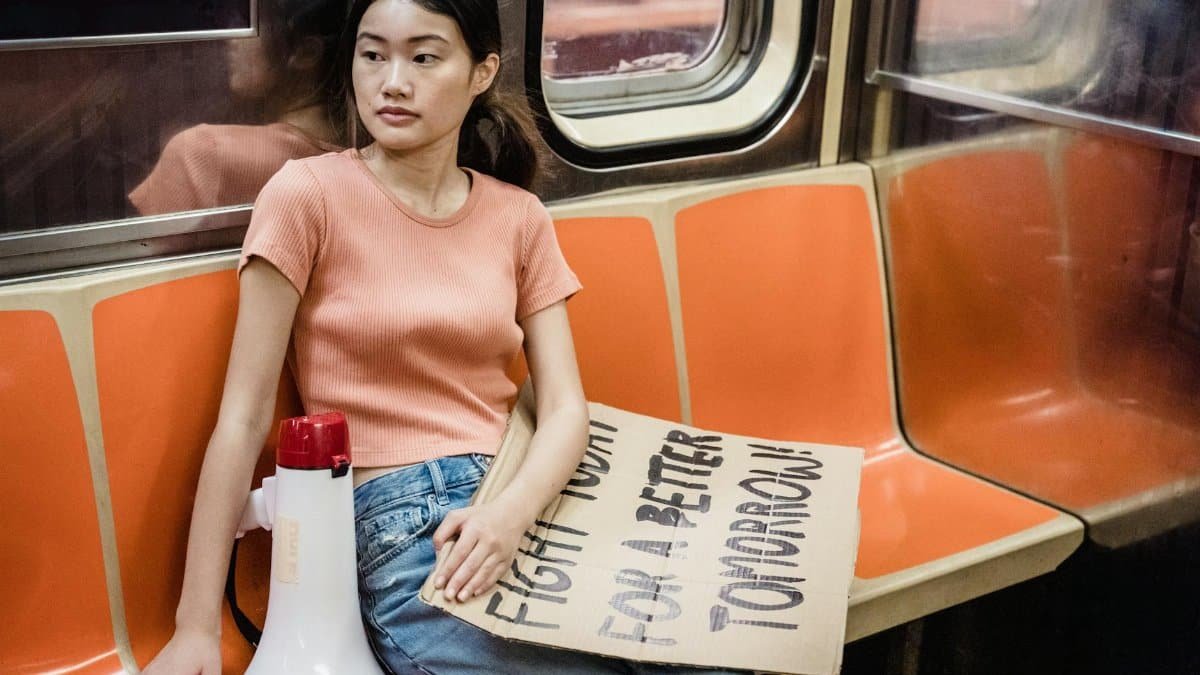 Young woman sitting on subway with protest sign, advocating change.