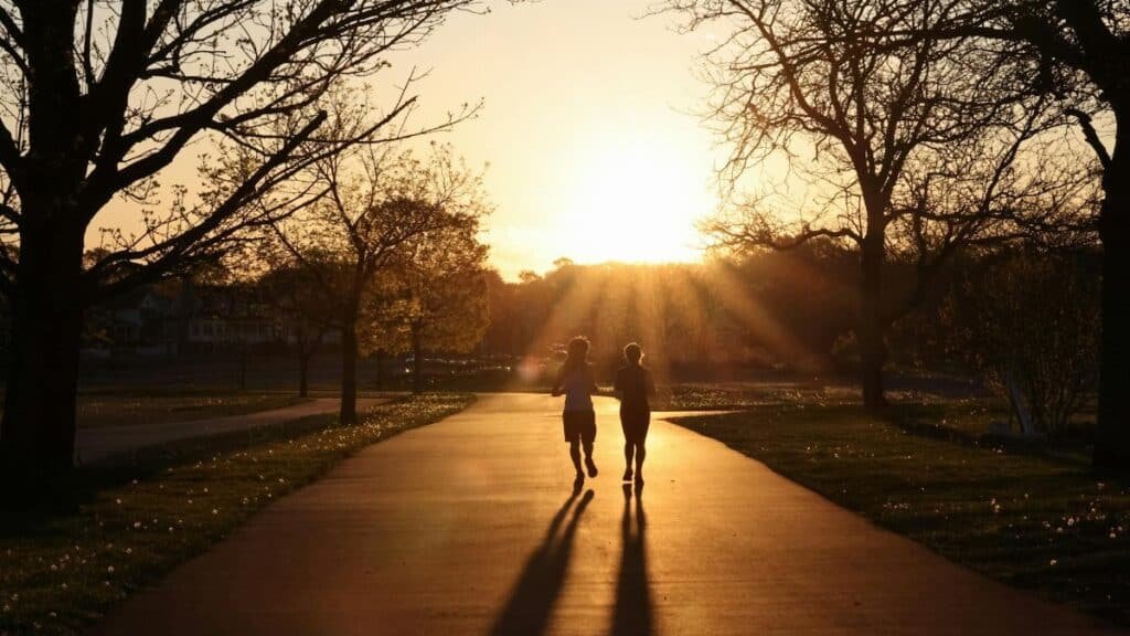 Silhouetted runners on a park path at sunrise in Stamford, CT, capturing the tranquility of early morning exercise.