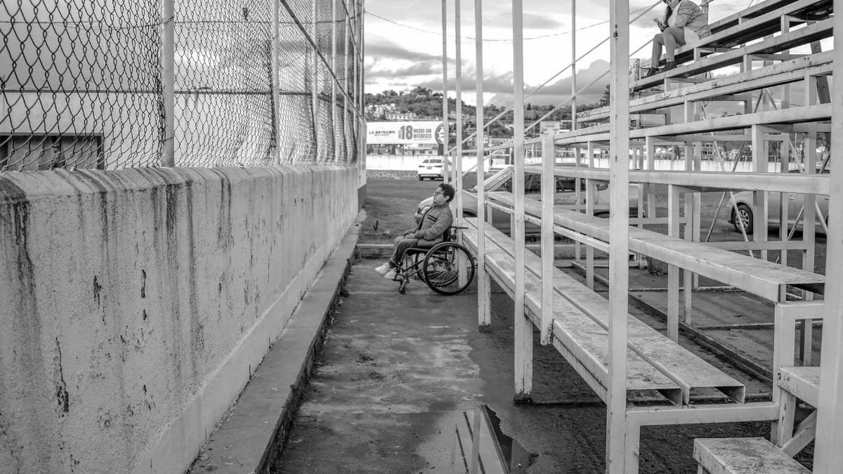 Black and white photo of a person in a wheelchair at bleachers, emphasizing solitude and accessibility.