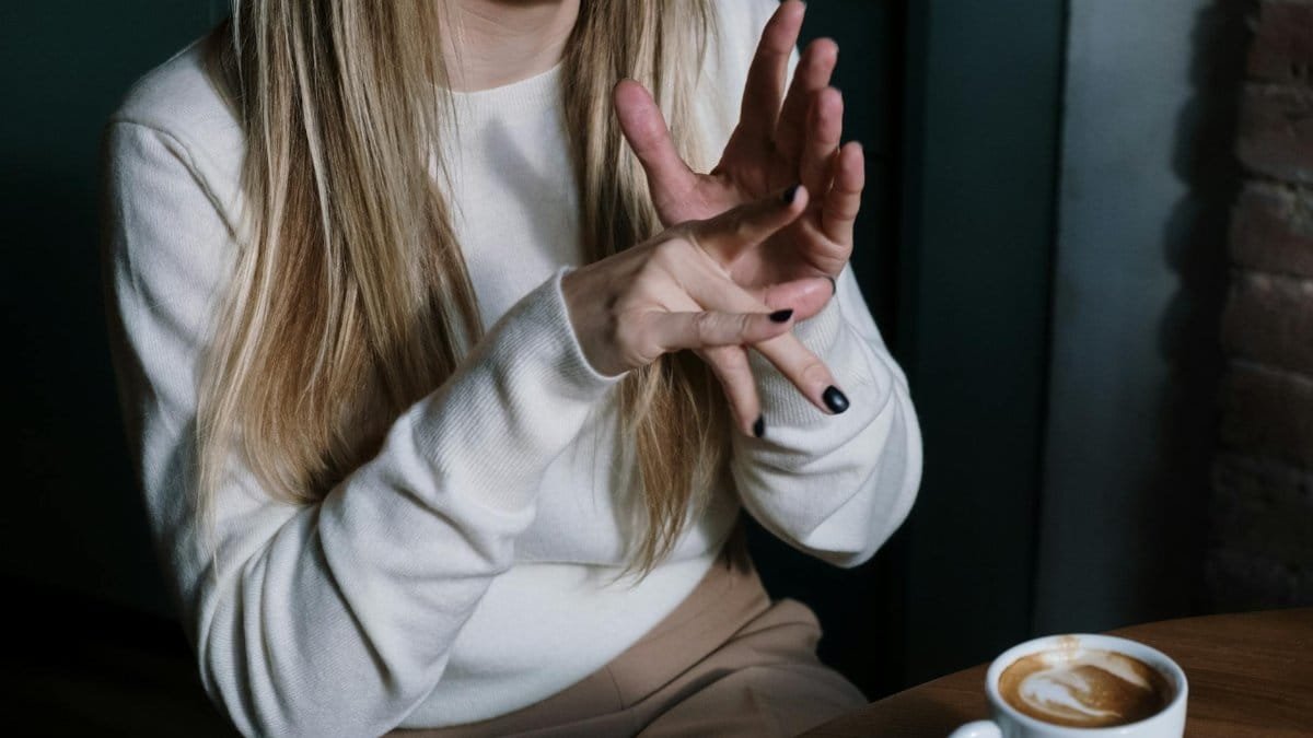Close-up of a woman gesturing in sign language with a latte in focus, illustrating communication and lifestyle.