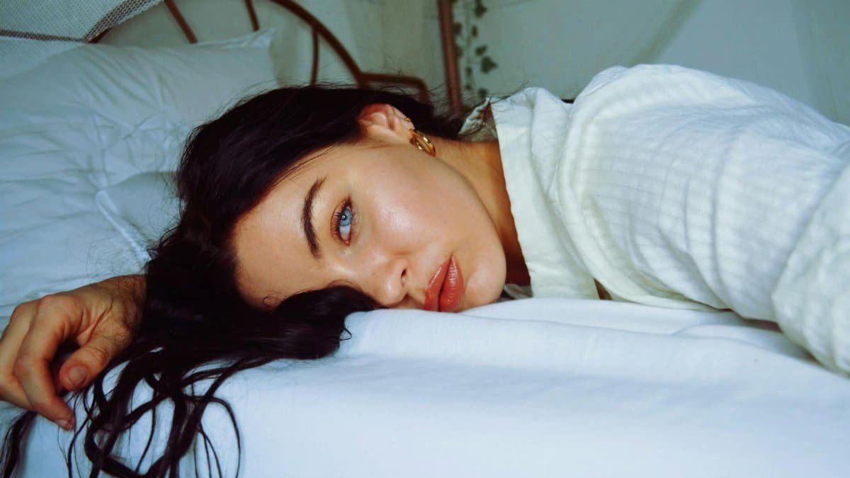 A serene portrait of a woman relaxing indoors, lying on a comfortable bed.