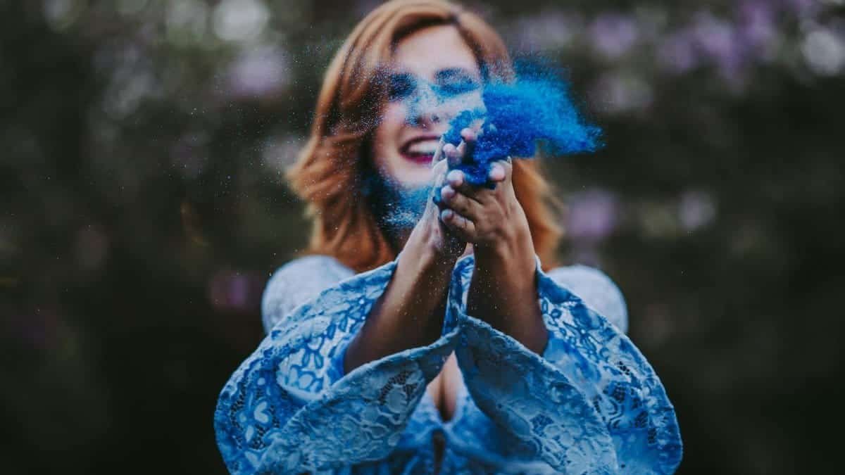 Smiling woman scattering blue powder outside, creating a vibrant and lively atmosphere.