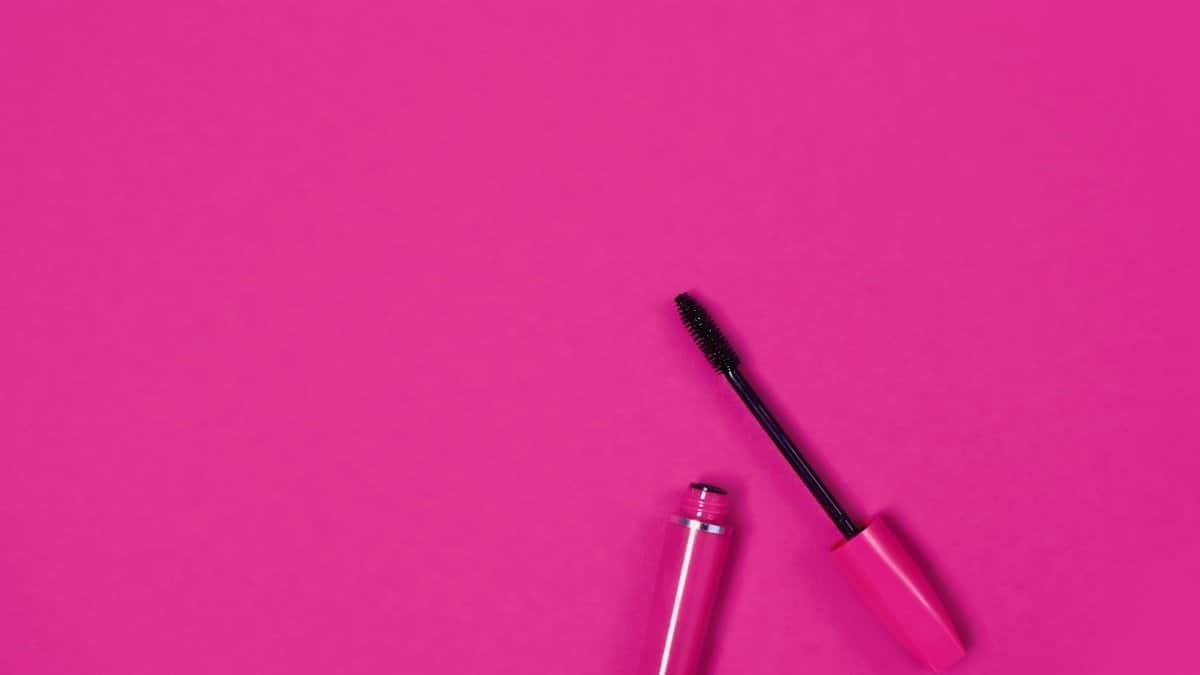 Close-up of an open mascara on a bright pink background, perfect for beauty and fashion themes.