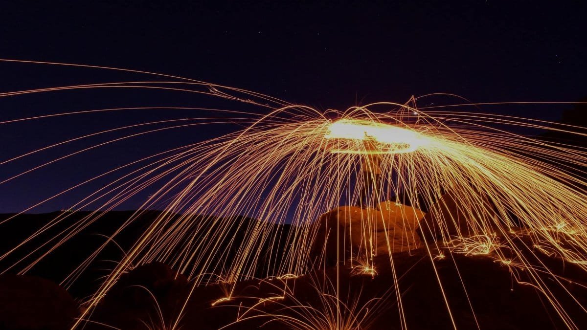 Vibrant long-exposure photo of steel wool sparks creating a dramatic light trail against the night sky.
