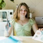 Teen girl crafting indoors, holding scissors, in a light-filled room, focused on creativity.