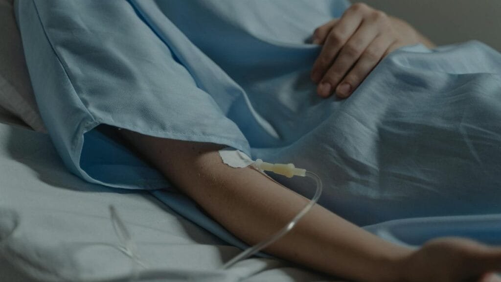 Close-up of a patient in a hospital bed with an IV drip attached to the arm.