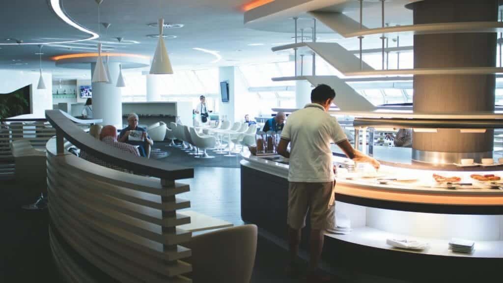 Stylish airport lounge with buffet and seating, featuring sleek interior design and contemporary furniture.