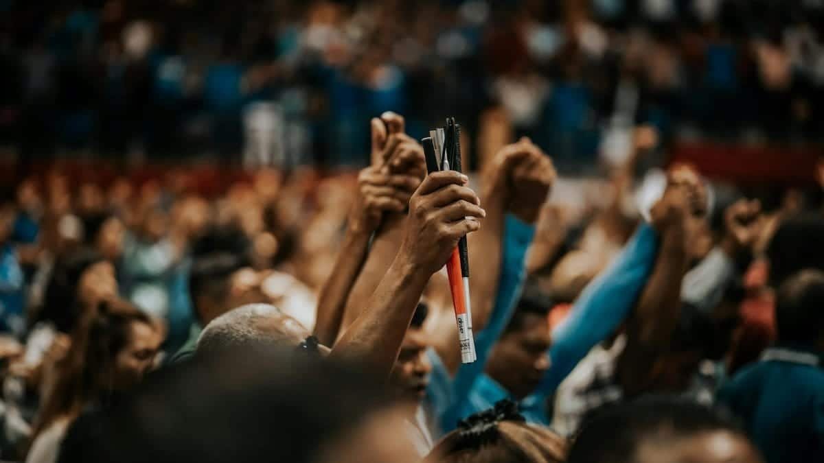 Energetic crowd with raised hands in a vibrant indoor gathering, symbolizing unity.