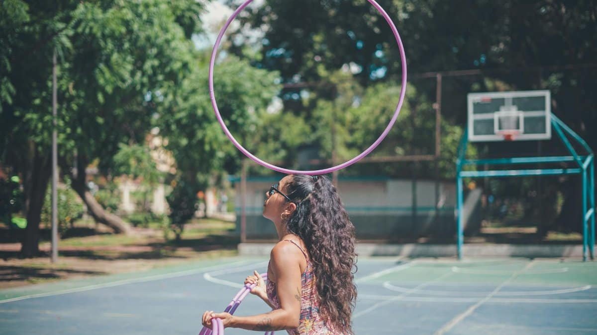 A young woman skillfully performing hula hoop tricks on an outdoor basketball court.