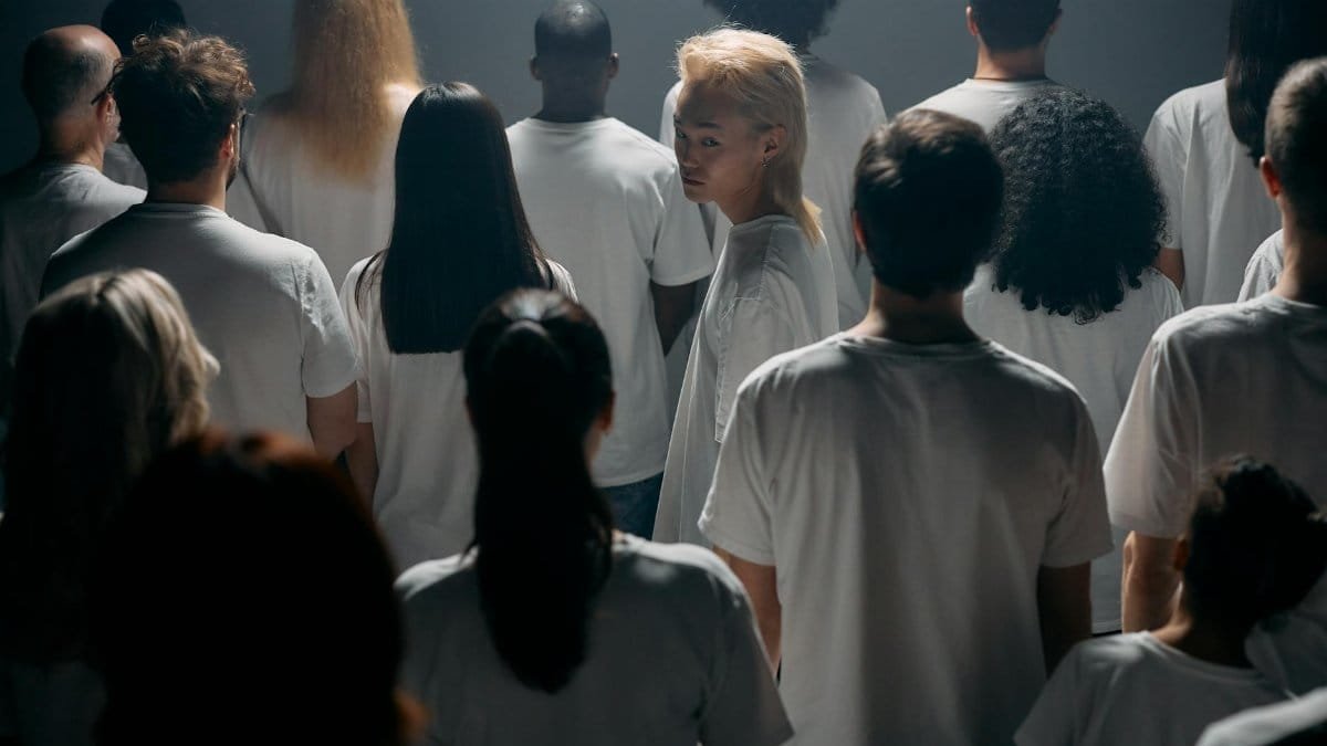 A diverse crowd stands together in a studio, exploring themes of individuality and social connections.