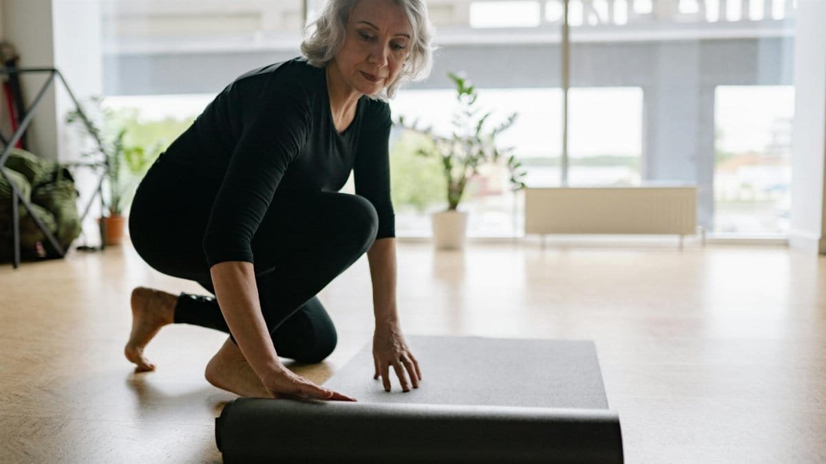 Senior woman setting up yoga mat in bright studio, preparing for exercise.