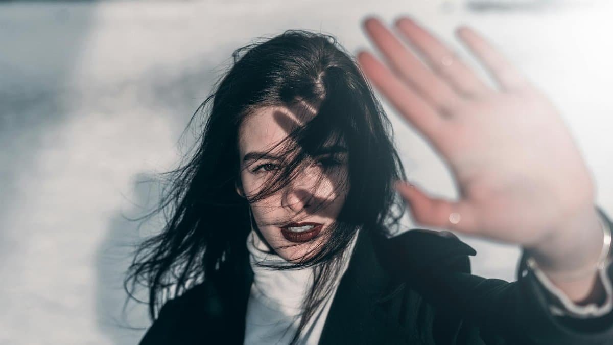 Close-up of a woman shielding her face from the sun with one hand raised, outdoors.