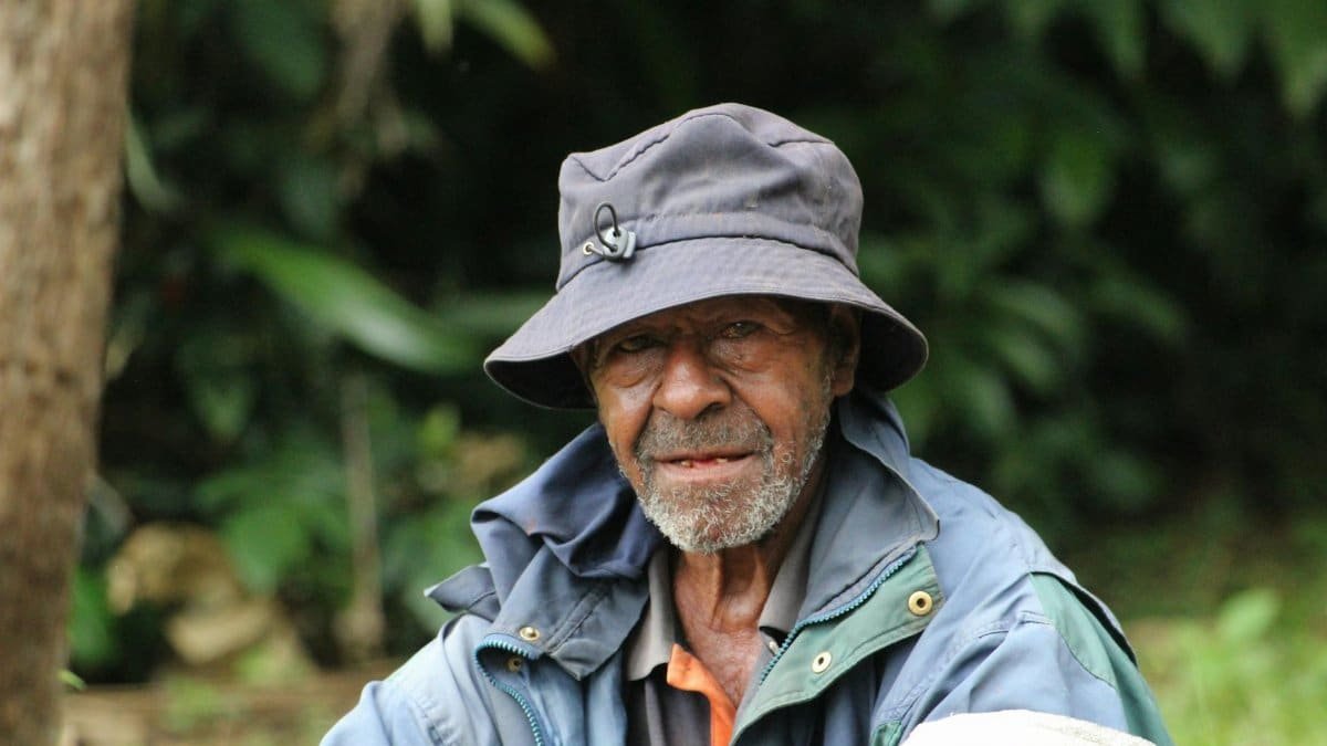 Portrait of an elderly man wearing a hat, sitting outdoors in Papua New Guinea.