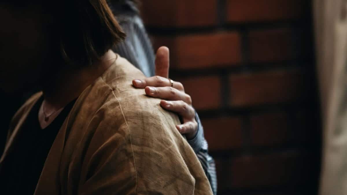 A close-up of a comforting hand on a woman's shoulder, symbolizing emotional support.
