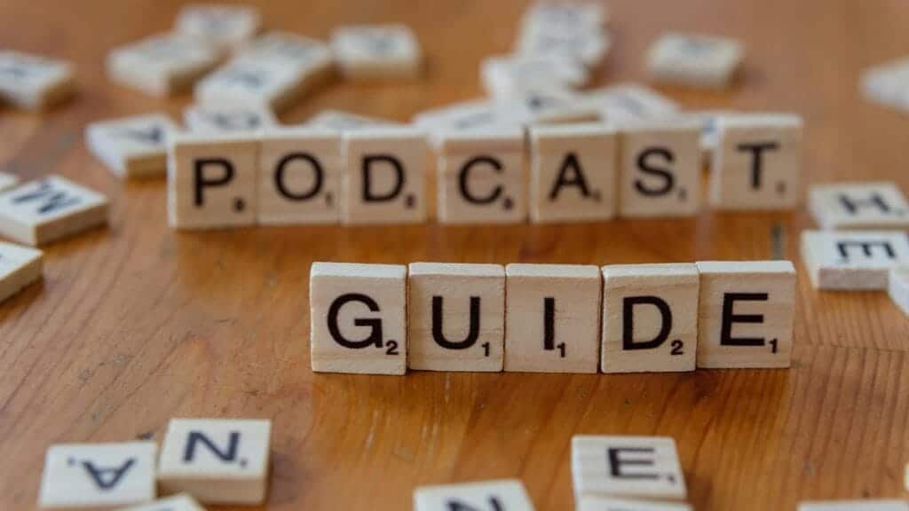Scrabble tiles forming the words 'Podcast Guide' on a wooden surface.