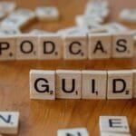 Scrabble tiles forming the words 'Podcast Guide' on a wooden surface.