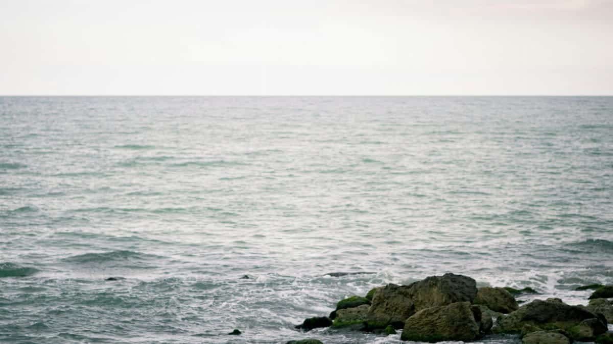 Calm ocean waves gently lap against a rocky shoreline under a bright sky.