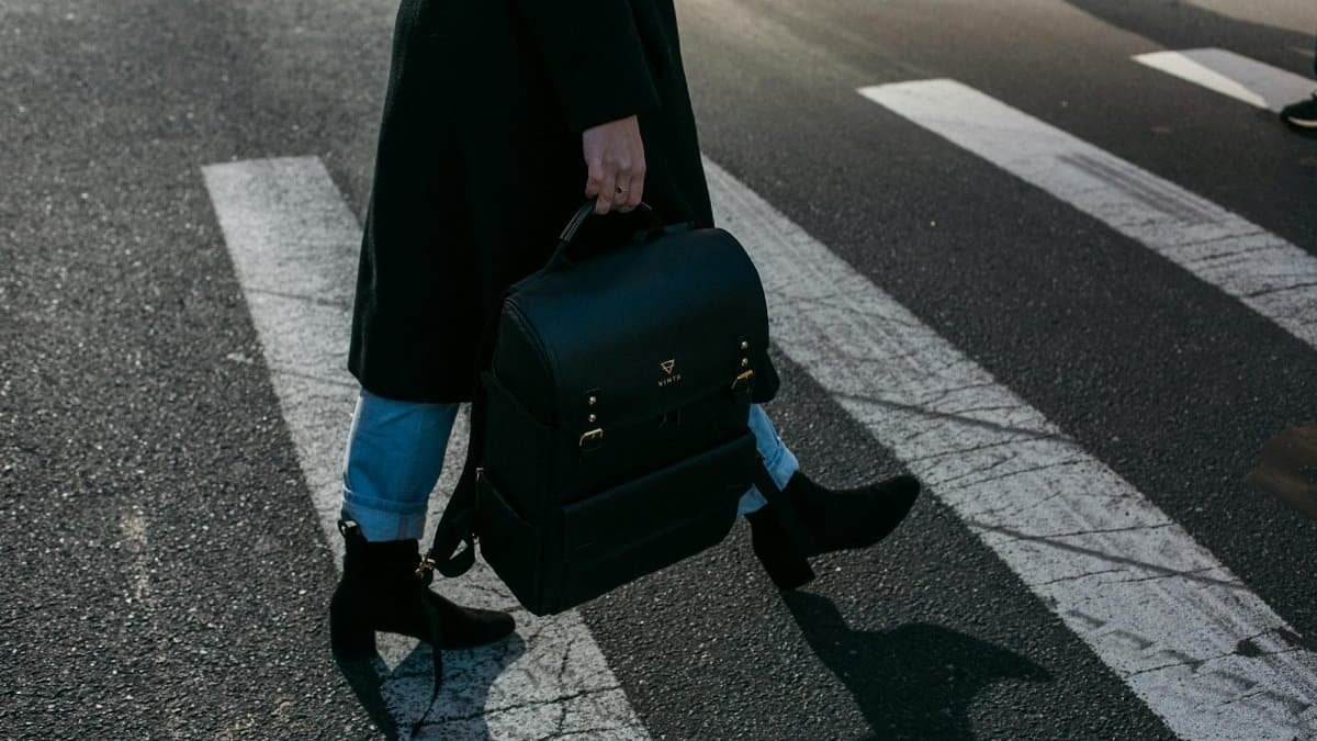 A person crosses a zebra crosswalk holding a stylish black bag in New York City.
