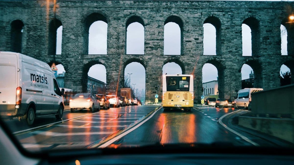 Evening traffic in Istanbul under a historic aqueduct, capturing city life and ancient landmarks.