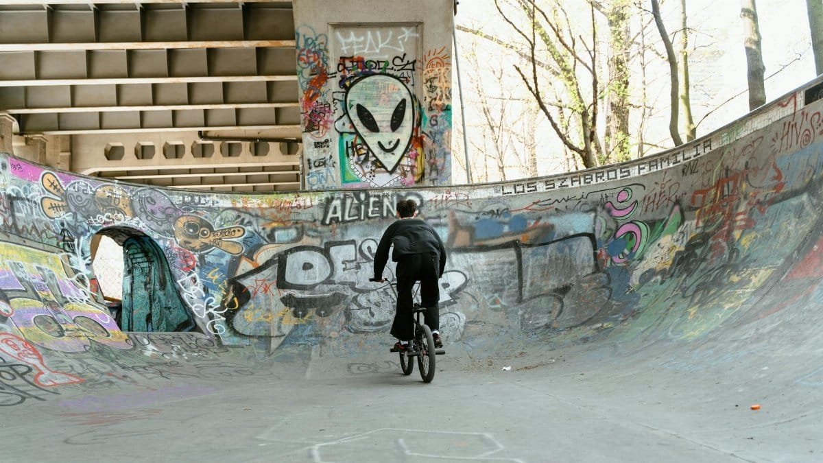 Action shot of BMX rider in urban skate park with vibrant graffiti walls, highlighting street culture.