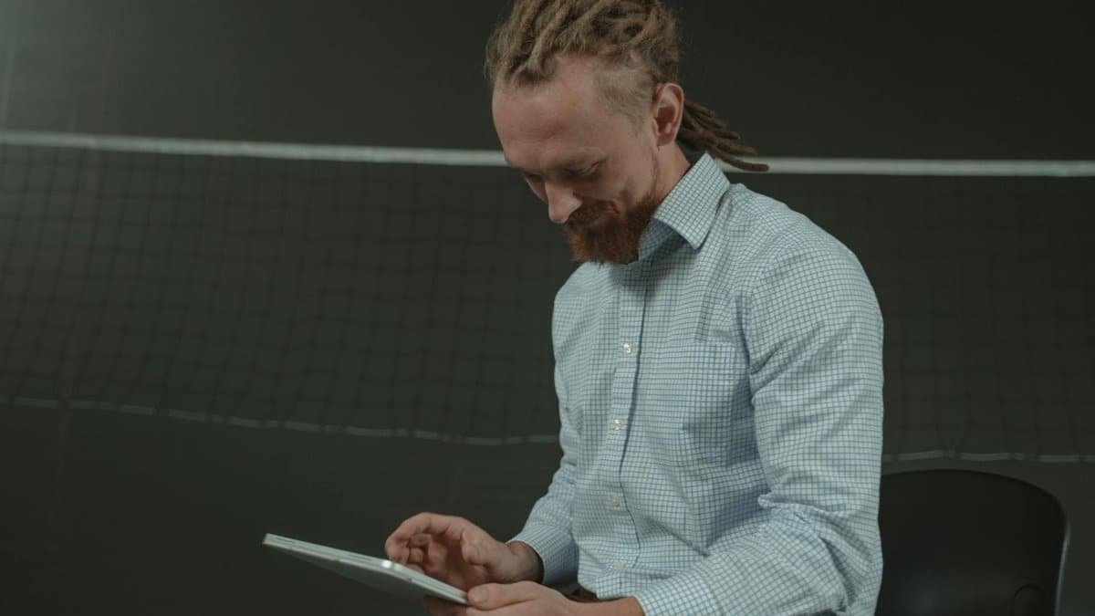 A man sitting with a tablet in an indoor sports hall looking focused.