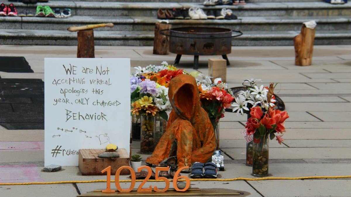 Outdoor installation highlighting social change with flowers, sculpture, and handwritten sign.