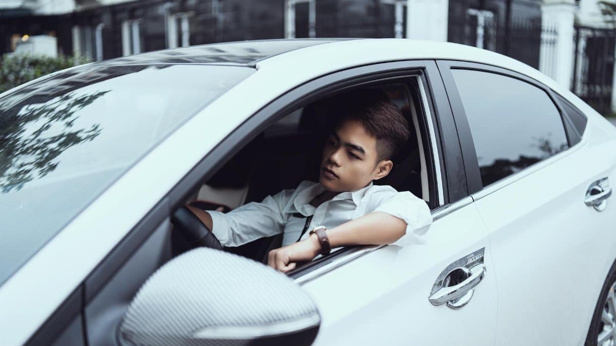 A young man in a modern white car, looking thoughtful while sitting in the driver's seat.