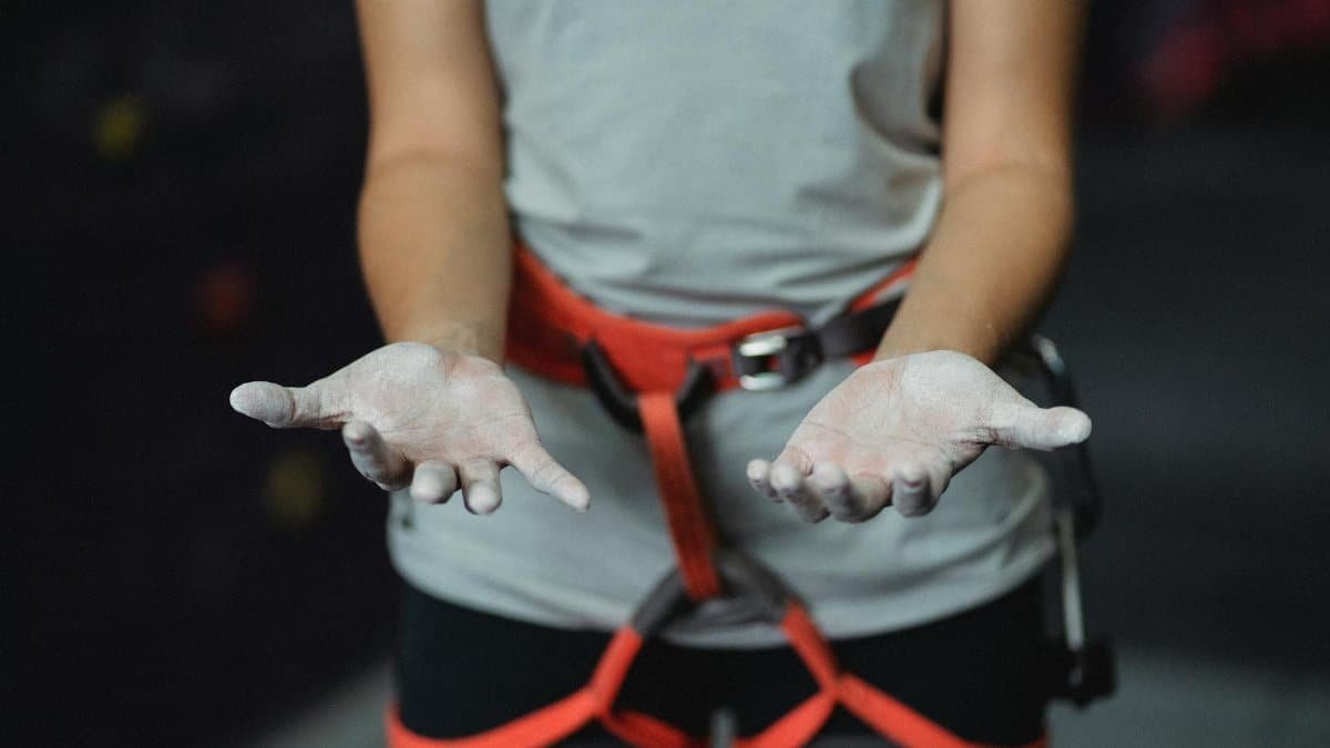 Crop anonymous slender female alpinist with safety harness demonstrating hands in talcum powder before practice