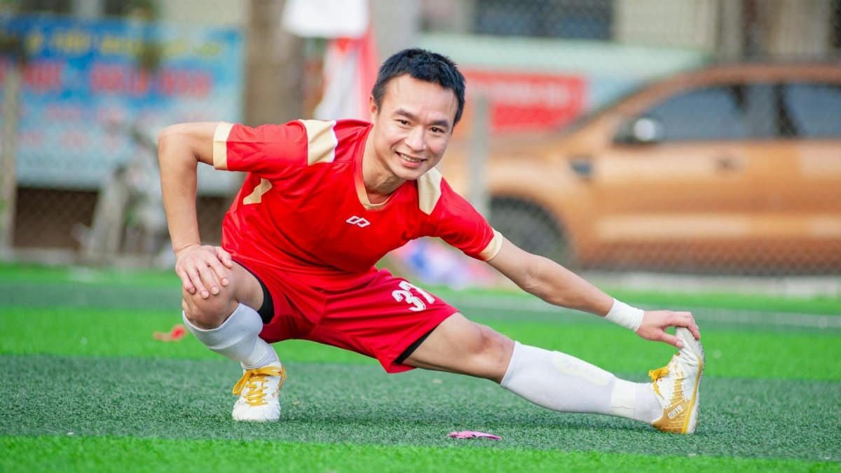 Smiling soccer player in red stretching on outdoor field in Hà Nội.