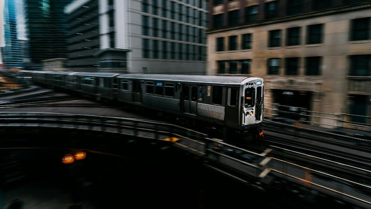 Fast-moving train on elevated tracks amidst downtown skyscrapers, showcasing urban transit.