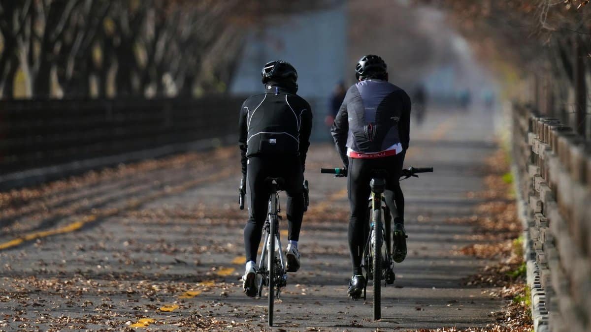 Two cyclists in active wear biking on a scenic pathway lined with autumn trees.