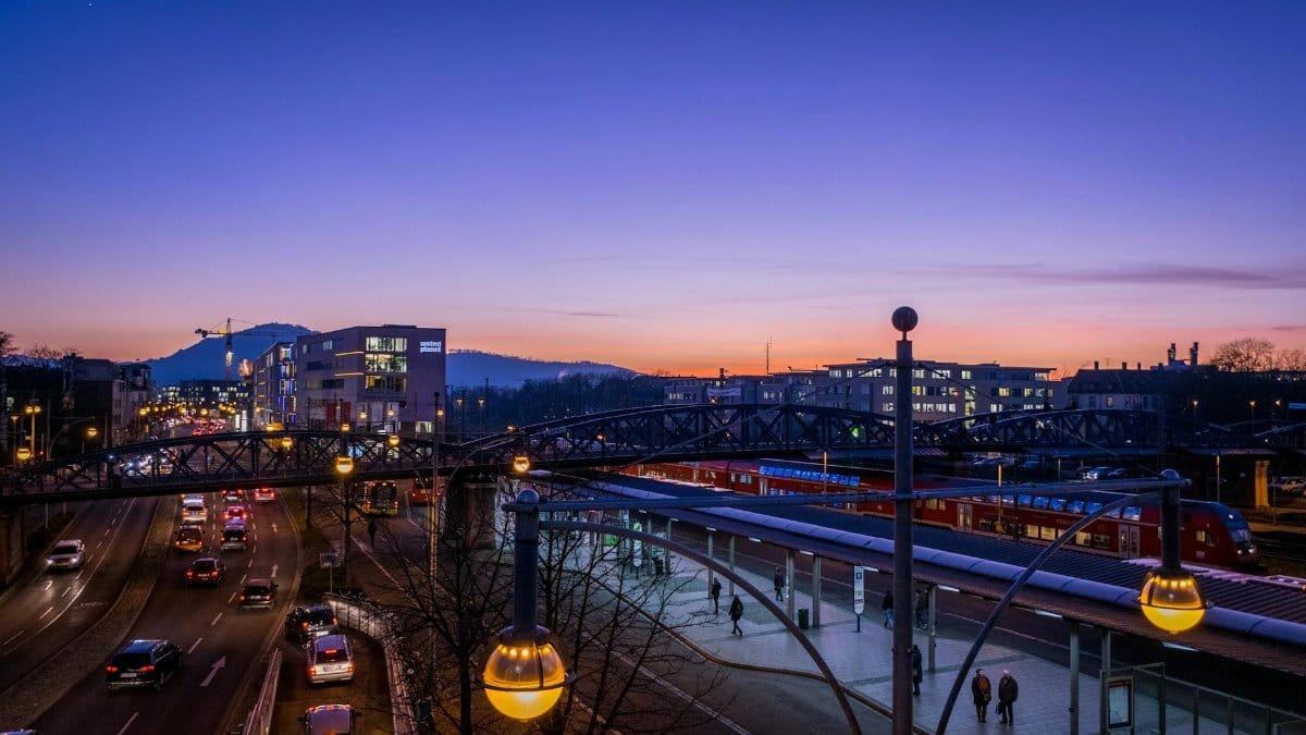 Elevated view of a bustling city street and station at dusk, featuring modern architecture and vibrant lights.
