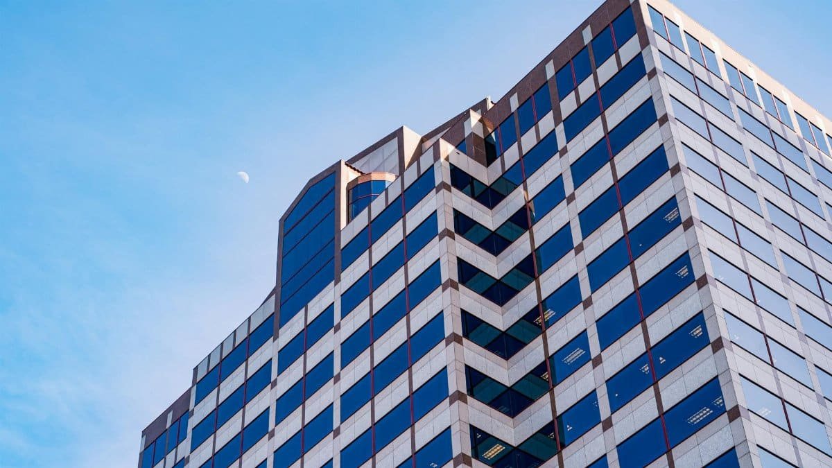 Low-angle view of a modern office building with geometric design and glass windows under a clear blue sky.
