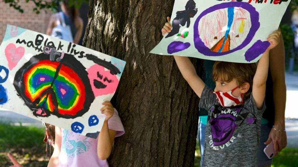 Children hold colorful Black Lives Matter signs in a peaceful outdoor protest.